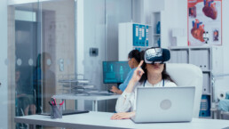 Young female doctor doing research in medicine with virtual reality headset on in private modern clinic. Nurse working in background and other medical staff walking by. Healthcare system hospital